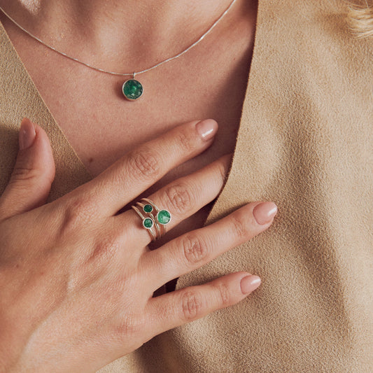 Silver 950 ring with three emeralds and matching emerald pendant on a woman's hand and neck.