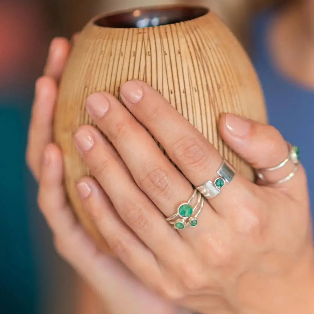 Handmade recycled silver rings with Colombian emeralds on a woman's fingers, holding a wooden object.