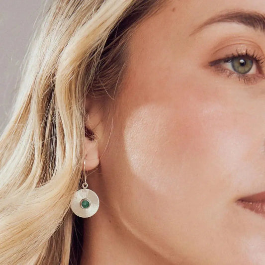 Handmade recycled silver coin earring with a vibrant Colombian emerald, worn by a woman.