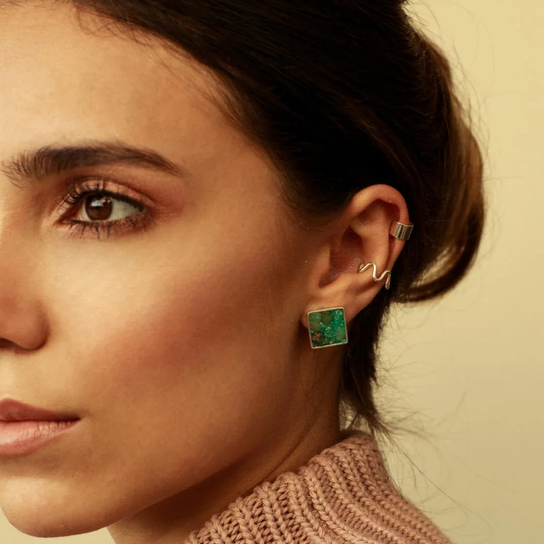 Woman wearing a square emerald earring in recycled silver 950, with two silver ear cuffs.