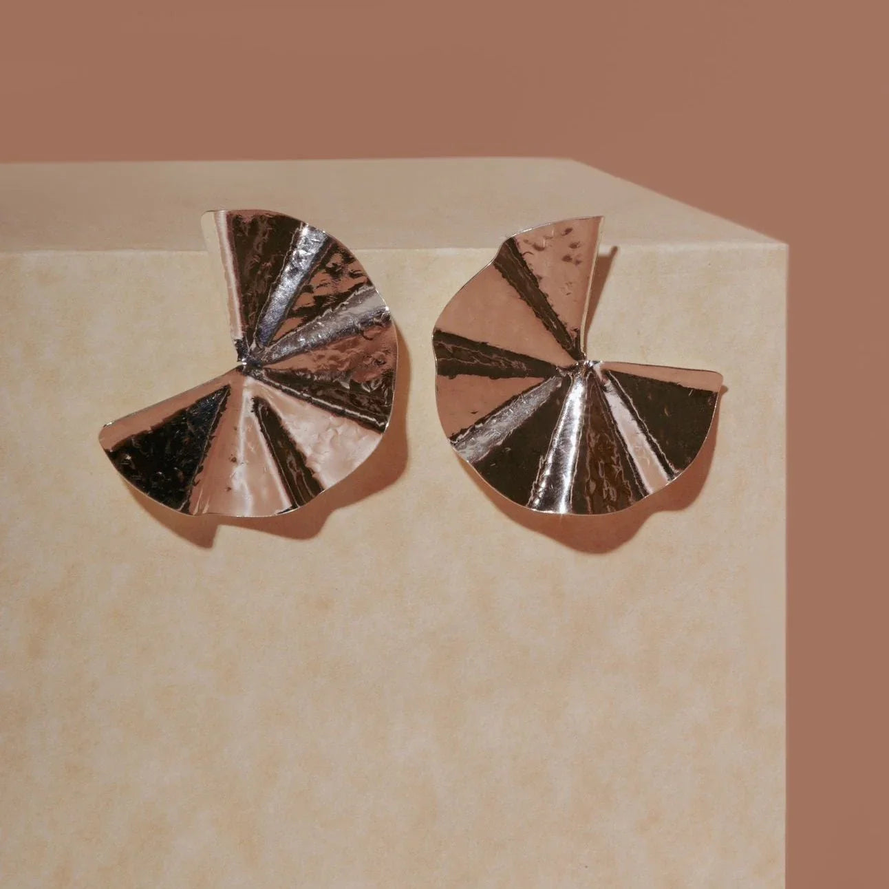 Hammered silver Pacman earrings, fan-shaped with textured and smooth segments, on a beige surface.