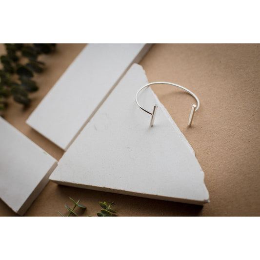 Minimalist silver 950 open cuff bracelet with two bar ends, displayed on white stone.