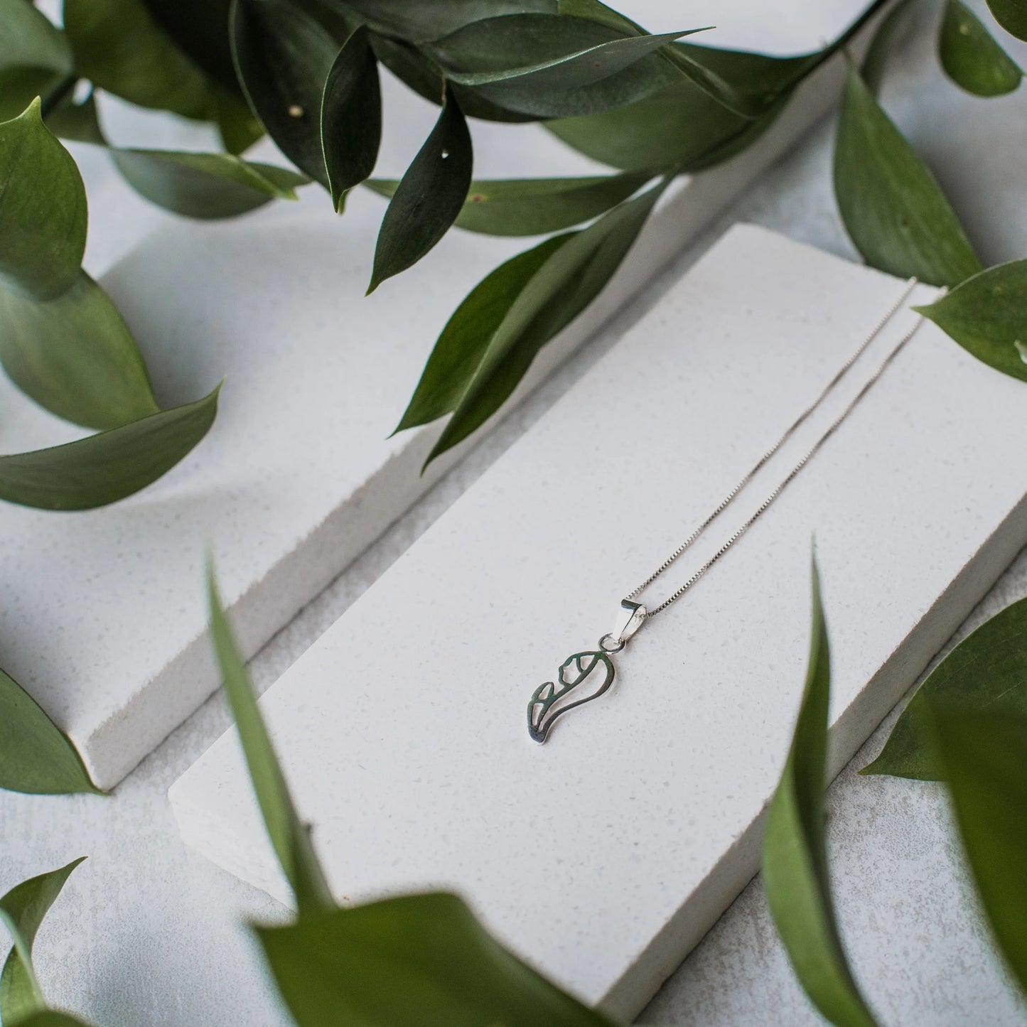 Silver 950 Virgin pendant necklace with a delicate chain, displayed on white blocks with green leaves.
