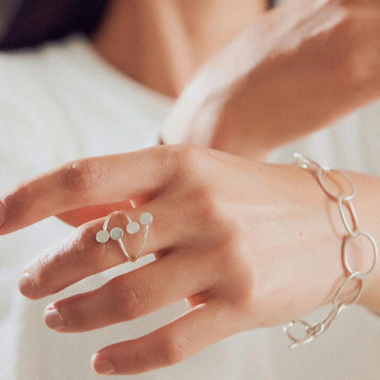 Silver 950 Constellation ring with four flat circles on a woman's hand, next to a silver chain bracelet.