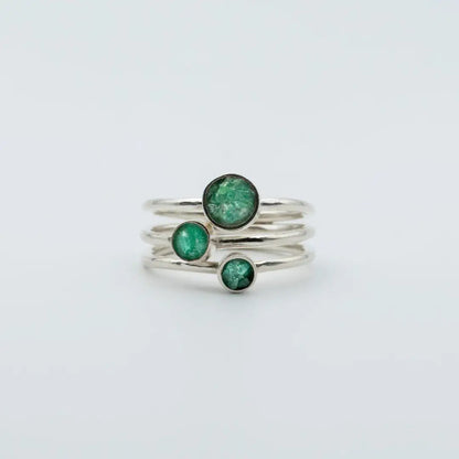 Three handcrafted recycled silver rings, each with a vibrant round Colombian emerald.