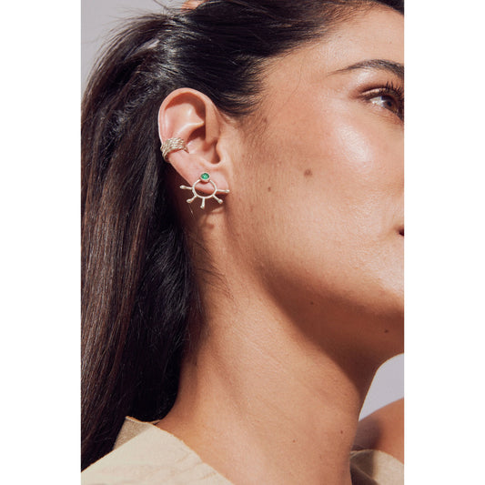 Silver sunburst earring with a green emerald center and a matching silver ear cuff on a woman's ear.