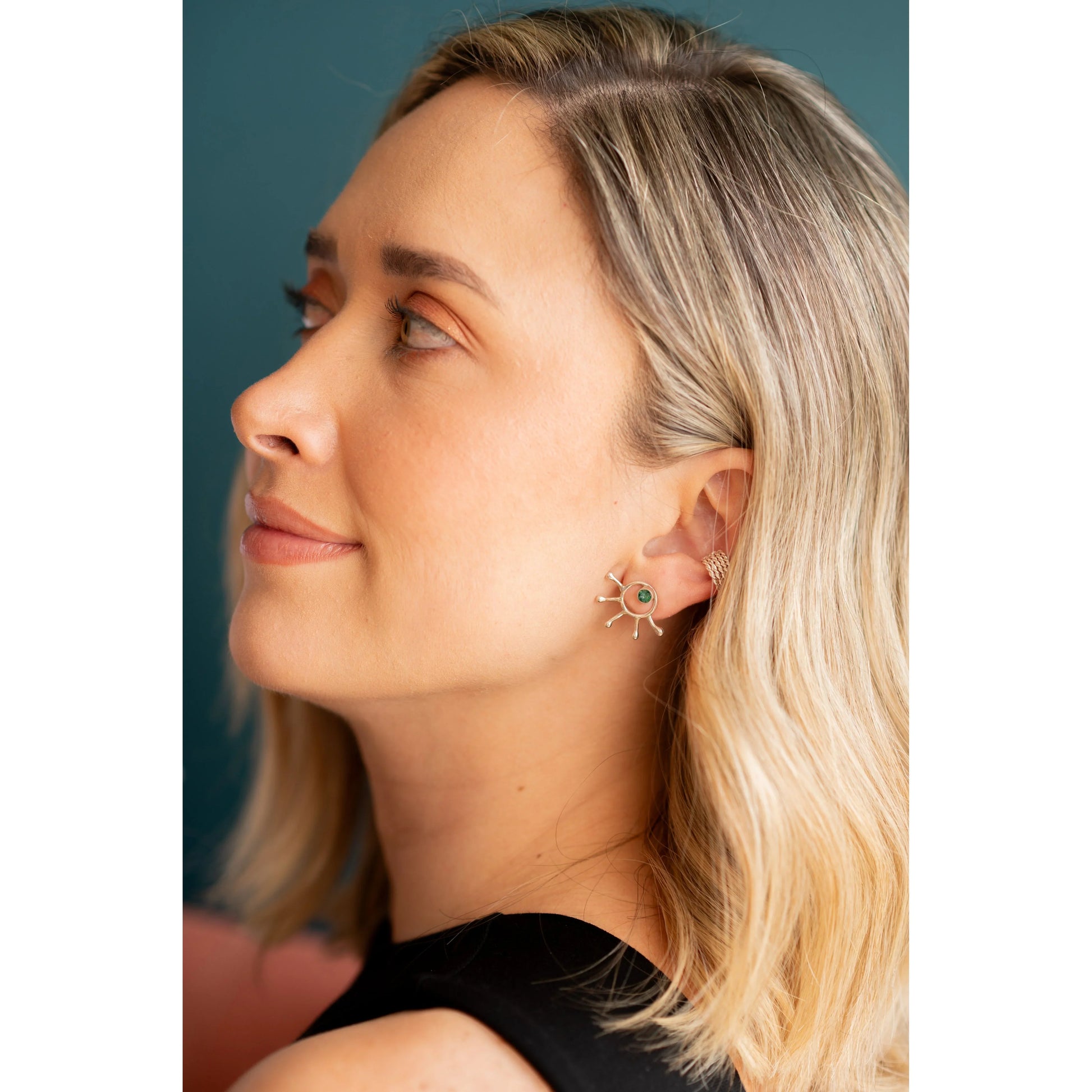 Blonde woman wearing a silver sunburst earring with a green emerald center and a matching ear cuff.