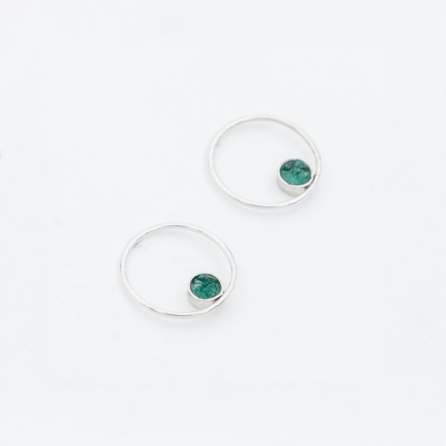 Pair of silver hoop earrings with small, round emerald stones set off-center.