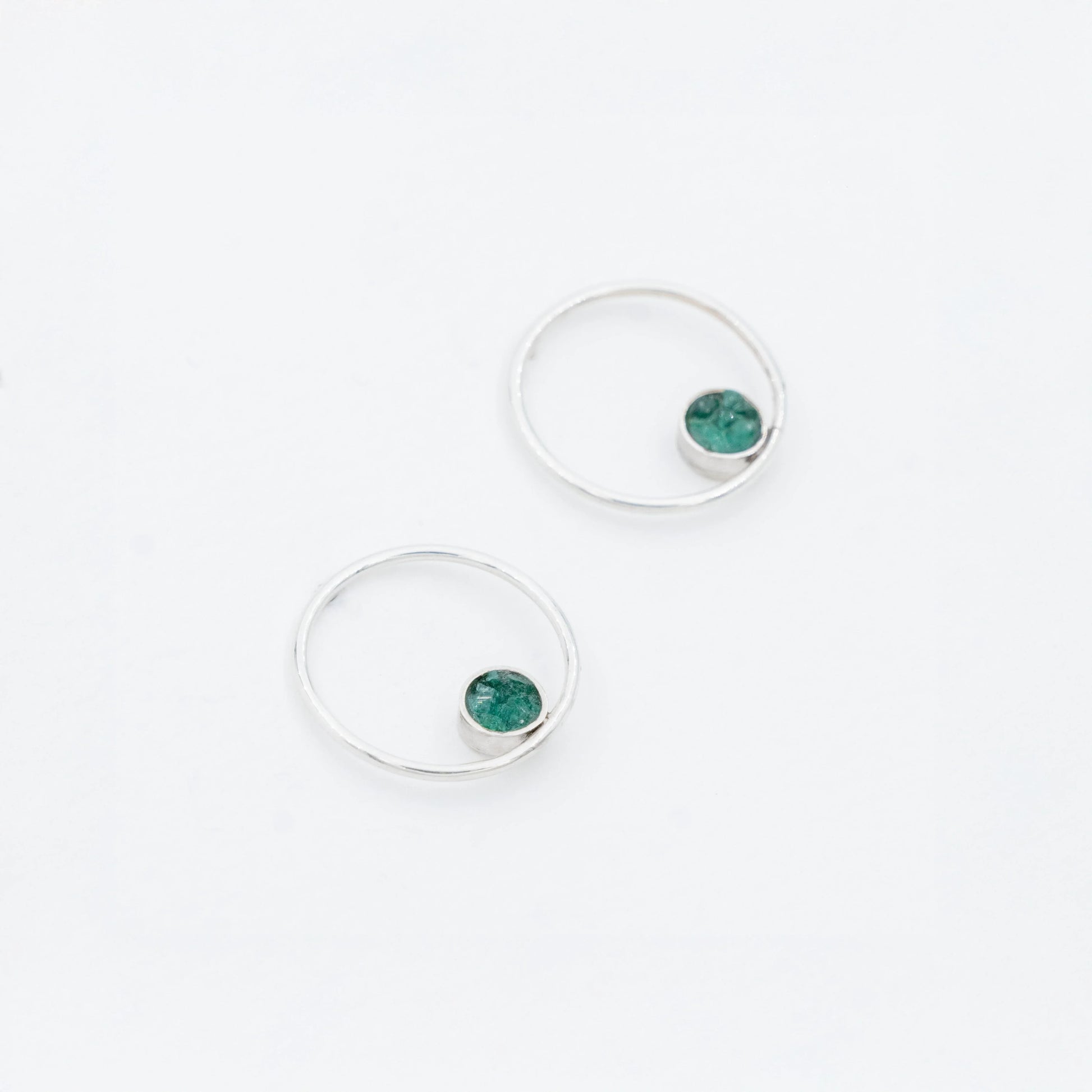 Pair of silver hoop earrings with small, round emerald stones set off-center.
