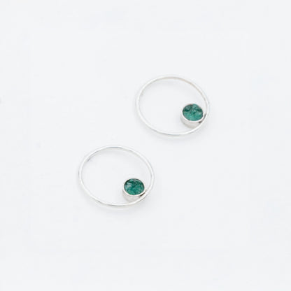 Pair of silver hoop earrings with small, round emerald stones set off-center.