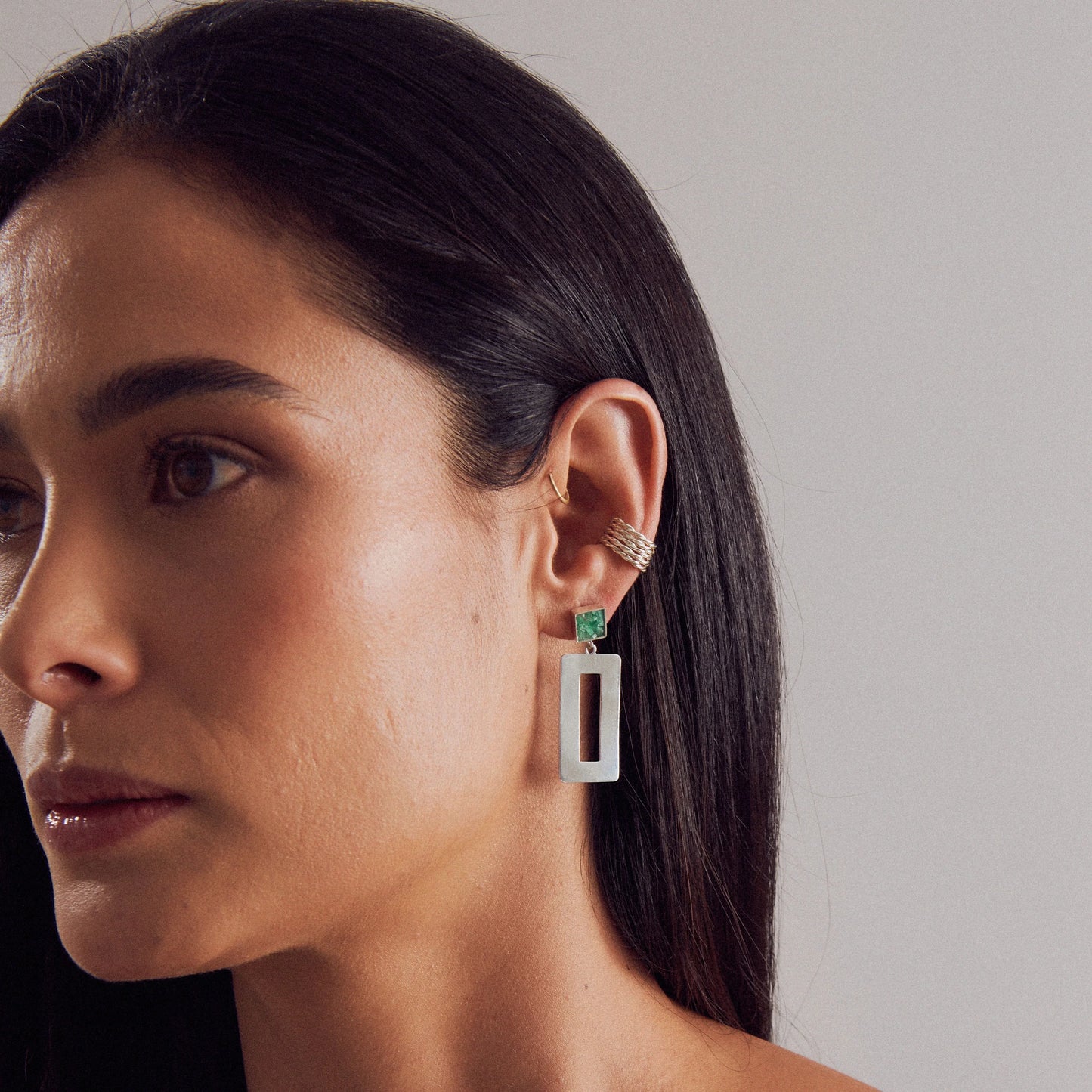 Silver rectangular dangle earring with a green emerald, worn by a woman.