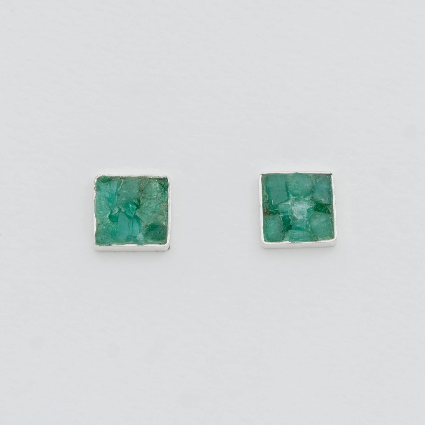 Square silver stud earrings with raw, vibrant green Colombian emeralds.
