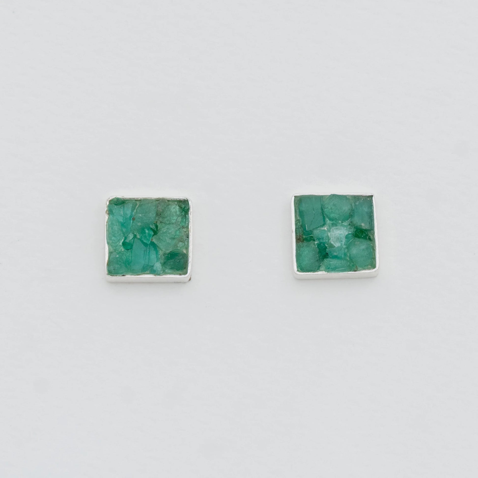 Square silver stud earrings with raw, vibrant green Colombian emeralds.