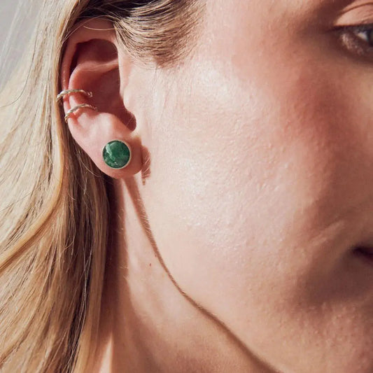 Round emerald stud earring in recycled 950 silver, worn on a woman's ear.