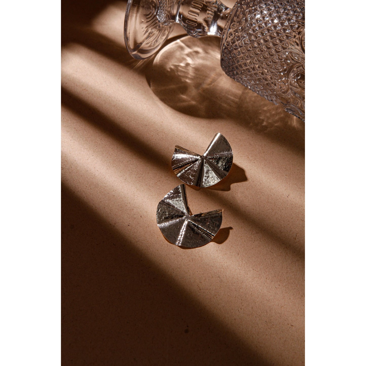 Hammered silver Pac-Man earrings on a brown surface with a decorative glass.