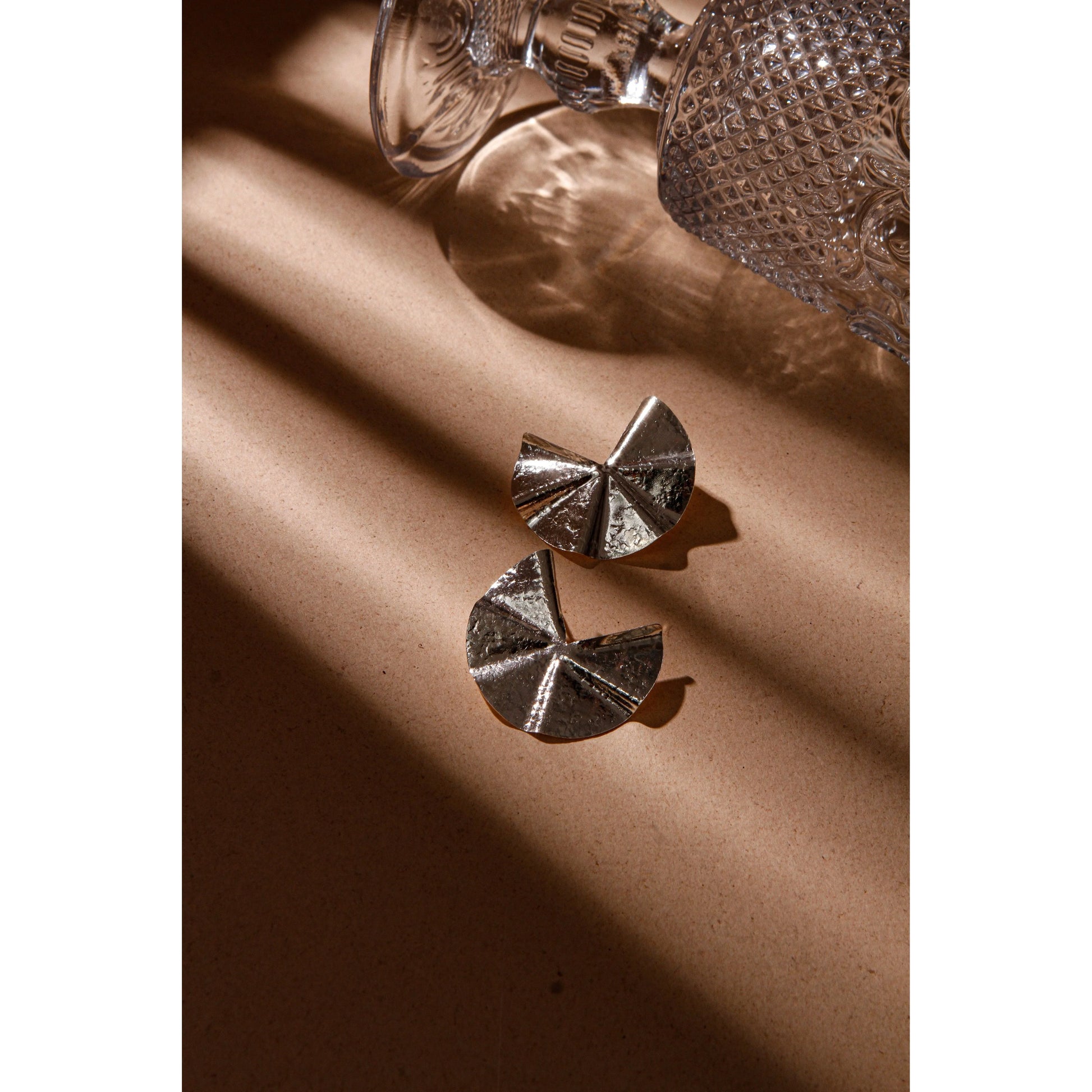 Hammered silver Pac-Man earrings on a brown surface with a decorative glass.