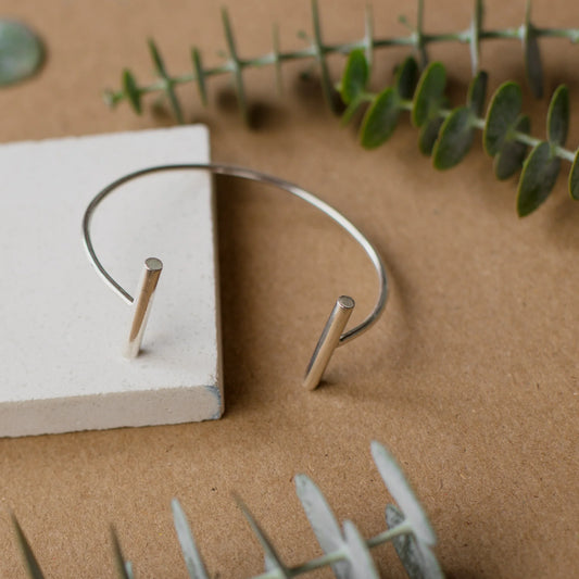 Sleek silver 950 cuff bracelet with two minimalist bar ends, on a natural background.