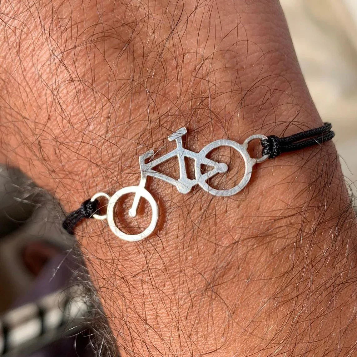 Silver 950 bicycle charm bracelet on a black cord, worn on a hairy arm.