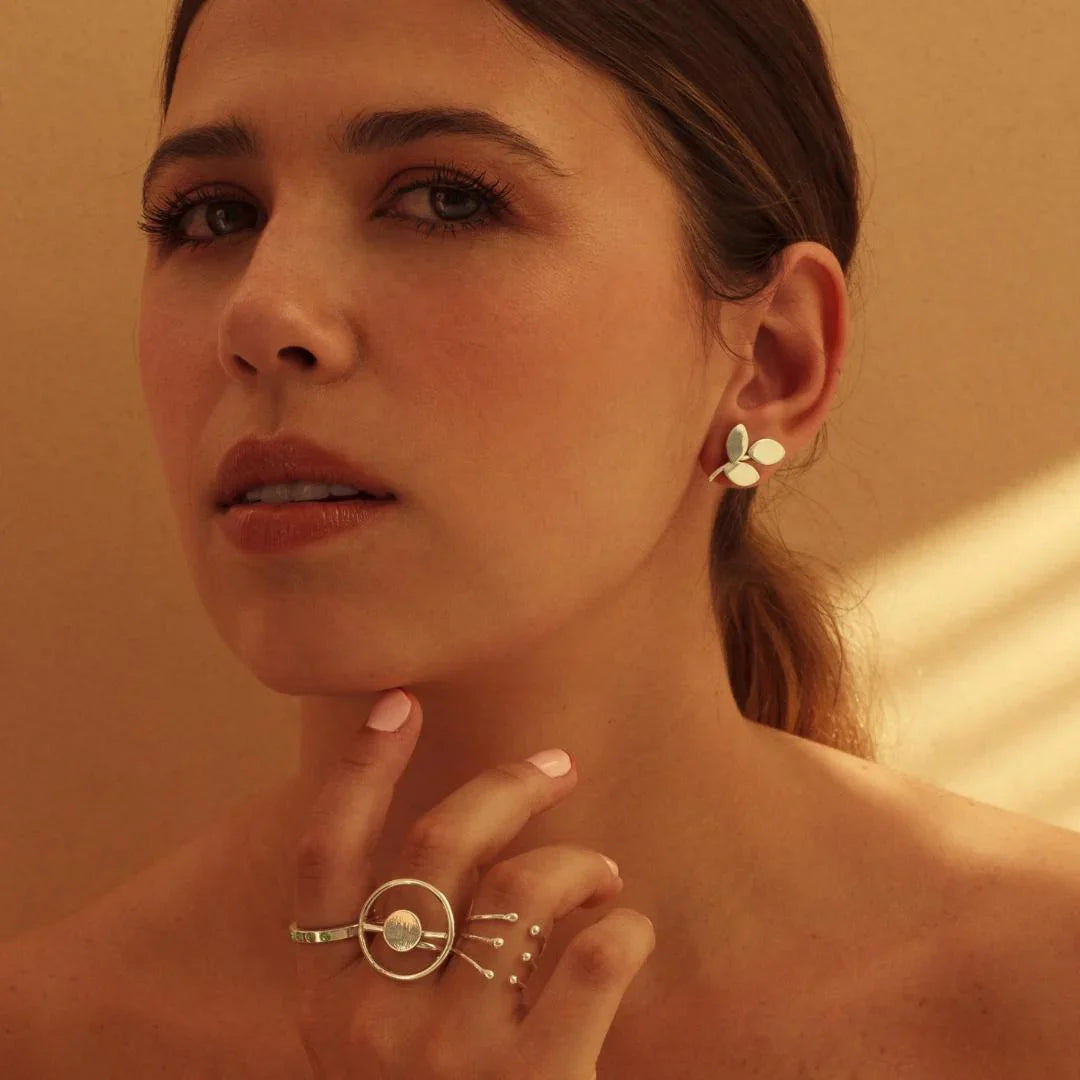 Woman wearing a unique silver Eclipse ring with a circular design and matching leaf-shaped earrings.